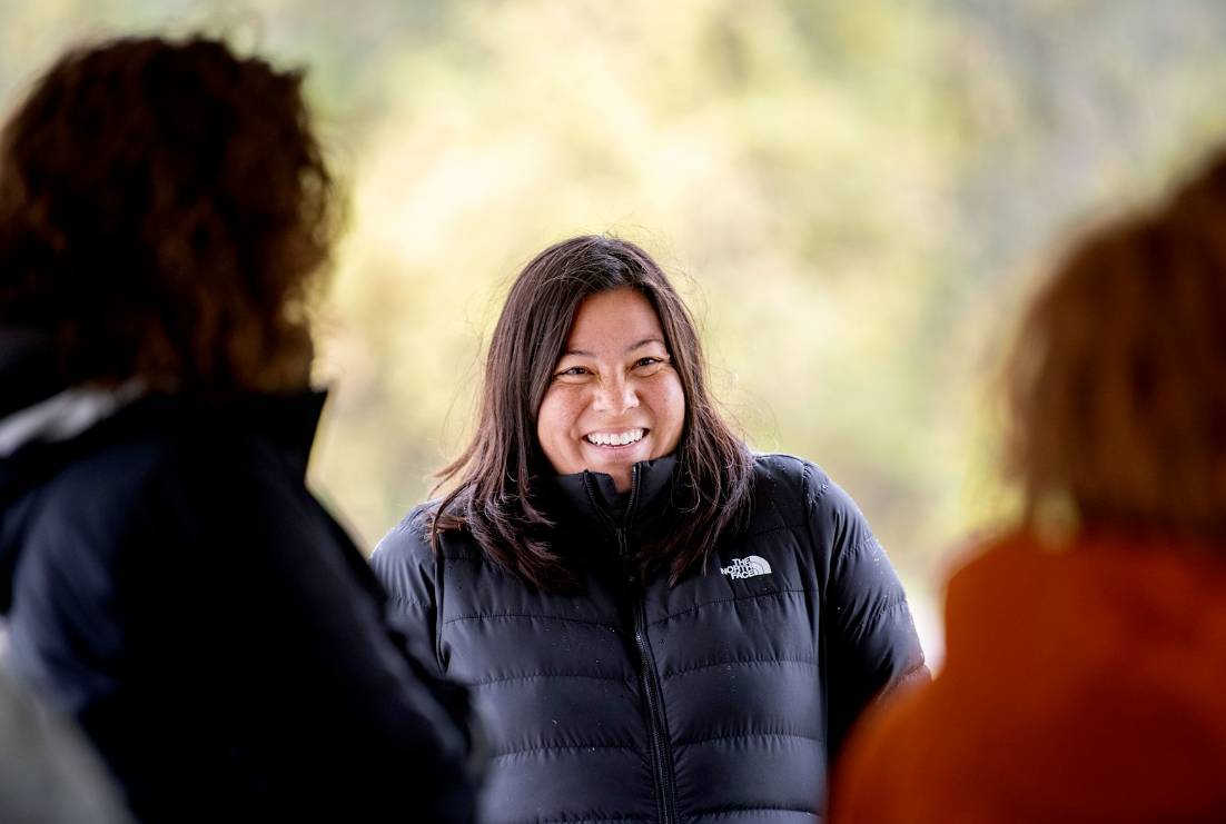 Person bundled in a coat smiling while talking to a group of people